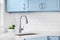 A kitchen sink detail shot with blue cabinets and subway tile backsplash.