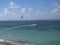 Kite surfer on blue water, with blue kite high in the air, and wispy blue sky in background