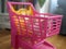 A kitten sitting in a pink toy shopping trolley