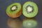 Kiwi fruit cut in half, reflected on the surface, isolated on a gray background.