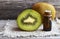 Kiwi seed oil in a glass jar with fresh halved kiwifruit on old wooden background.