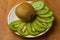 Kiwi single whole and sliced in pieces in a white plate and on a wooden board