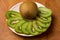 Kiwi single whole and sliced in pieces in a white plate and on a wooden board