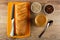 Knife, bread on cutting board, bowls with sunflower seeds and raisin, jar with peanut butter, spoon on table. Top view