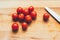 Knife and cherry tomatoes lie on a wooden board.Vibrant cherry tomato and kitchen knife on a wooden chopping board lying on gray