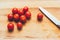 Knife and cherry tomatoes lie on a wooden board.Vibrant cherry tomato and kitchen knife on a wooden chopping board lying on gray