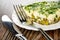 Knife, fork on plate with slice of omelet with parsley and green peas on wooden table