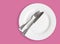 Knife and fork on white plate on pink background - top view photo