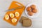 Knife, halves of peeled eggs on cutting board, pieces of bread, eggs in plate on wooden table. Top view