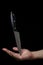 Knife on the hand on a dark background. The knife balances on the hand against a black background.