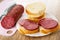 Knife, piece of sausage on cutting board, slices of bread, sandwiches with sausage in plate on wooden table