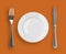 Knife, plate and fork on orange top view