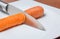 Knife slicing carrot in a white plate over table