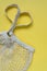 Knitted string bag on a yellow background. Heart shaped handles