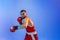 Knockout punch. Male boxer in red uniform and boxing gloves training  on blue background in neon. Strength