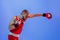 Knockout punch. Male boxer in red uniform and boxing gloves training isolated on blue background in neon. Strength