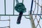 Knotted sports rope hanging from crossbar of horizontal bars on background of racks, rope ladders and climbing nets on playground