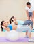 She knows her workouts will pay off. Young woman doing a sit up during a pilates class with the help of an instructor.