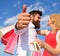 He knows how to make her happy. Couple with shopping bags cuddle blue sky background. Man with beard shows thumb up