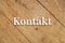 `Kontakt` white text on a wooden background. Translation: Contact