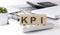 KPI written on a wooden cube on keyboard with office tools