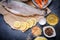 Kraft paper raw fish with lemon slices lies on a dark gray table top on a white plate. A variety of different pepper is on the