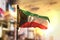 Kuwait Flag Against City Blurred Background At Sunrise Backlight