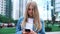 Kyiv, Ukraine - June 5, 2019: beautiful teenage millenial girl using smartphone on the modern city street skycrapers