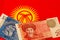 Kyrgyzstan currency banknotes and coins and the national flag as the background