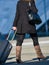 La defense, France- April 09, 2014: Business traveler walking down the street and pulling suitcase.She wears tall boots, a black