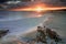 La Pelosa beach in Sardinia at sunrise with a sunburst and rocks in the foreground