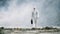 Lab technician in a mask and chemical protective suit, walks on dry ground with a tool box through toxic smoke