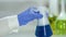 Lab worker in gloves stirring flask with blue boiling liquid, pharmacology