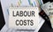 LABOUR COSTS text written on the notebook with chart,calculator and dollars