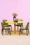 Laconic interior of the dining room. Yellow round table and green leather chairs, vase with flowers on the table. Isolate on pink