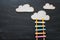 Ladder made of colorful chalks and pencils next to clouds over blackboard background.