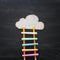 Ladder made of colorful chalks and pencils next to clouds over blackboard background.