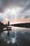 Lady aged 20-25 standing on a wooden pier by a pond watching the sunset over the town of Oostende, western Belgium. Dramatic red-