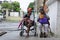 Lady, Blind Man beside disabled Beggar in wheelchair at Church yard Gate Portal