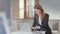 Lady in business suit, glasses works on laptop, smiles at camera