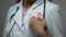 Lady doctor attaching pink ribbon to white medical suit, breast cancer awareness