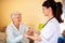 Lady doctor handing a glass of water to elder woman nursing home occupant