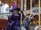 Lady dressed up as a witch in purple garment riding on the carousel