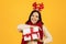 lady holding Christmas gift box posing in festive antlers, studio