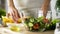 Lady holding lemon piece and olive oil for dressing, organic salad bowl on table