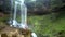 Lady holds yoga pose with hands above head by waterfall