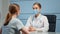 Lady medical consultant in facial mask and white coat examines blonde patient talking