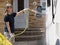 A lady motorhome owner cleans her recreational vehicle with a hose pipe.Spray can be seen coming from the pipe as lady cleans van
