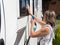 A lady motorhome owner cleans her windows.She has a spray gun with blue cleaning liquid in one hand