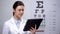 Lady optometrist checking results in tablet and smiling to camera, technologies